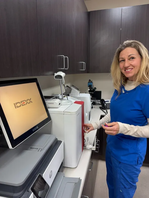 Veterinary technician in scrubs operating IDEXX diagnostic equipment at Animal Medical Center of Pleasanton.